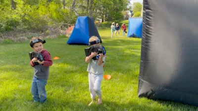 Two boys laughing as they aim laser taggers at an outdoor birthday party in Glen Mills, Delaware County, PA
